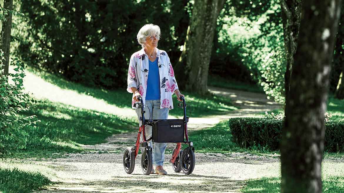Donna anziana con deambulatore, passeggia nel parco sotto gli alberi